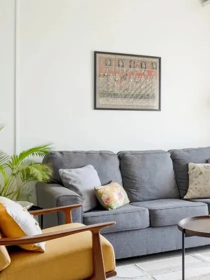 A close-up of the living room seating, showing the pop of yellow from the accent chair and the traditional Indian artwork on the wall.