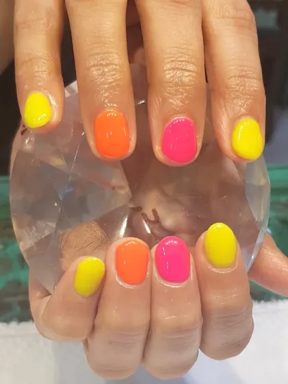 Summer nails ready to shine. This fun manicure features alternating shades of neon yellow, orange, and pink for a bright and cheerful look.