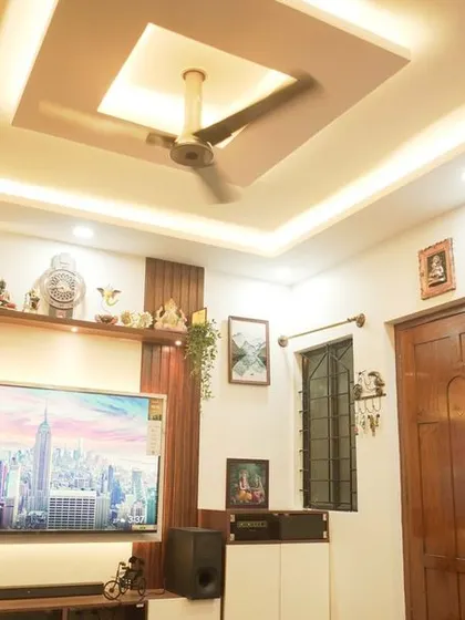 A detailed look at the living room's false ceiling and TV unit. The square-in-square ceiling design and the combination of wood and white on the media console create a balanced and modern look.