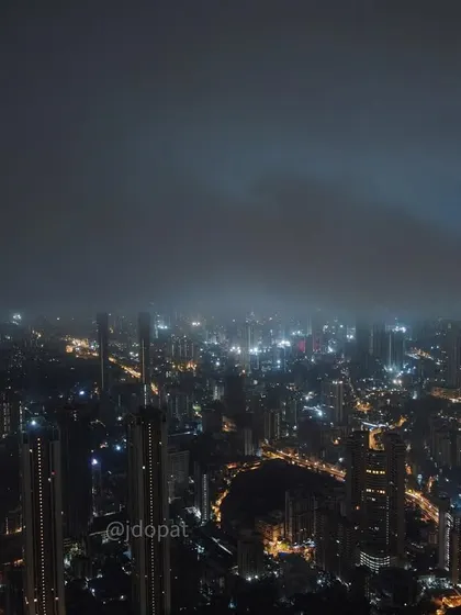 A drone's perspective of Mumbai at night, with the city lights partially obscured by low-hanging monsoon clouds.