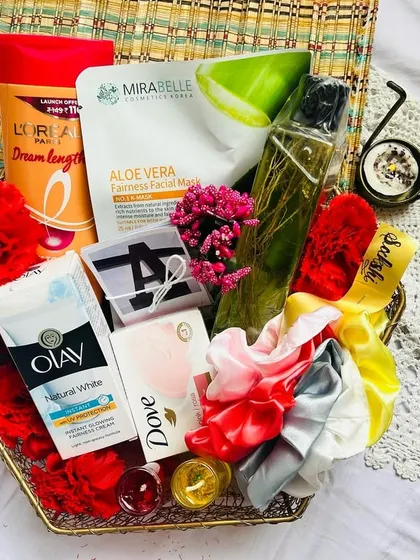 An overhead view of a self-love hamper, showing the mix of products like a Mirabelle face mask, nourishing scalp oil, and Olay moisturizer. The colorful scrunchies and candles add a pop of fun.