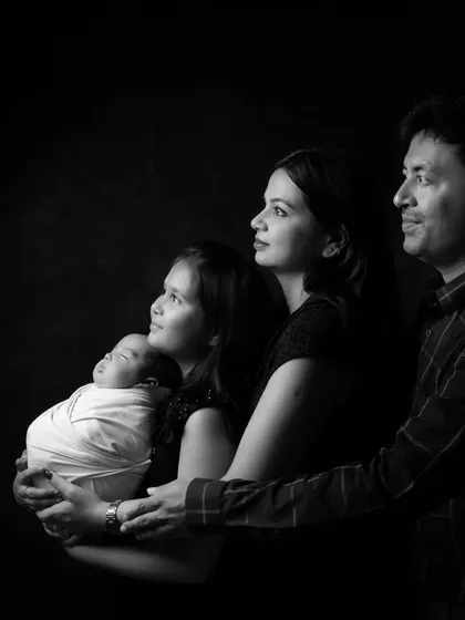 A timeless black and white family portrait capturing the profile of a father, mother, older sister, and newborn baby.