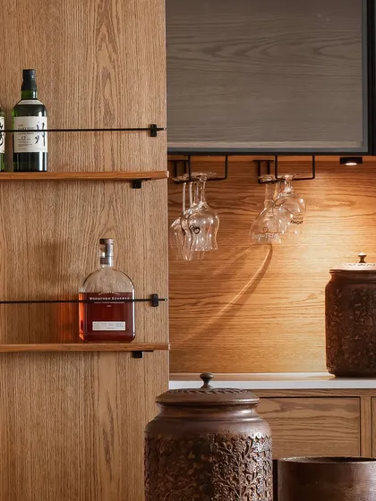 This custom bar unit, hidden behind a wooden cupboard, is designed for effortless entertaining. It features dedicated shelving for bottles, integrated glass holders, and warm under-cabinet lighting, blending seamlessly into the dining space when not in use.