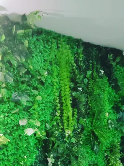 A close-up view of a lush green wall, showing how different types of artificial leaves and hanging plants are combined. This dense arrangement ensures no part of the original wall shows through.