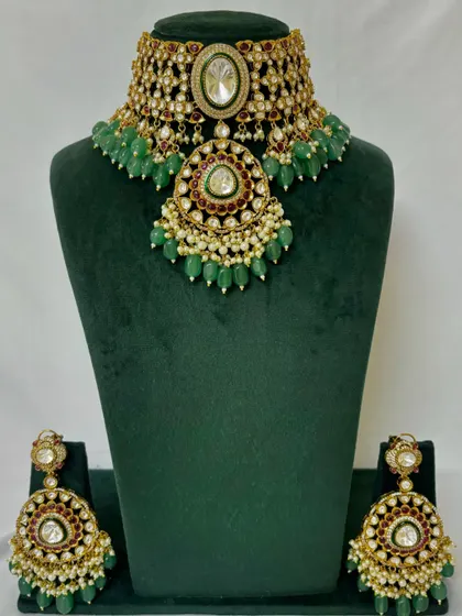 A full view of a heavy bridal choker with a large pendant and green bead drops. This rental set comes with matching oversized earrings.