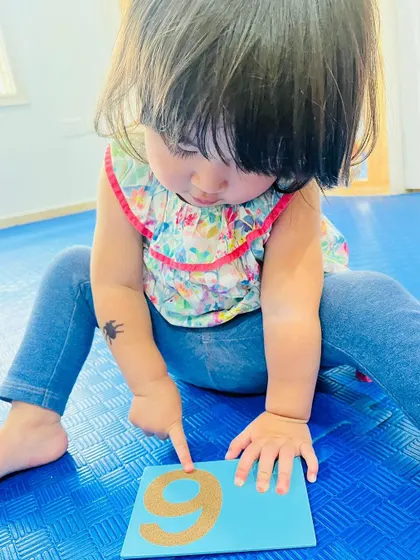 A close-up of a toddler's finger tracing a sandpaper number. These multi-sensory activities are highly effective for early learners.