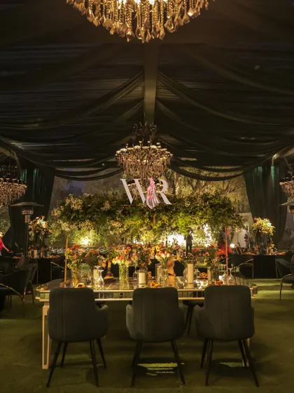 A moody, atmospheric shot of the main table, with the dark, draped ceiling and chandeliers creating a dramatic frame. This perspective emphasizes the grandeur and scale of the overall design.