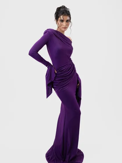 A high-fashion pose in a draped purple gown. The messy, wet-look updo adds a touch of undone elegance to the structured and glamorous dress.