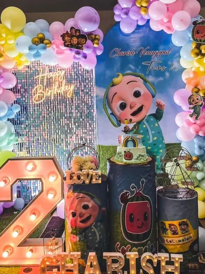 A grand Cocomelon party for Charish's second birthday, this setup includes a shimmering sequin wall, a large light-up number '2', and plenty of colorful balloons and characters.