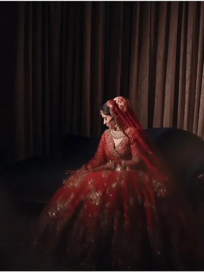 A dramatic, low-light portrait of the bride seated, her red lehenga glowing in the dark. This shot is pure cinematic artistry.