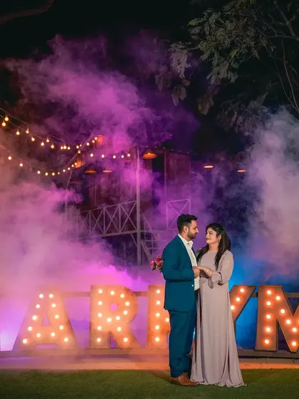 A romantic portrait of a couple standing before the 'MARRY ME' sign, enveloped in a cloud of purple smoke. This highlights our expertise in using atmospheric effects for night photography.