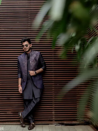 The groom leans against a wooden wall, looking cool and relaxed in his sunglasses and Mehendi outfit.