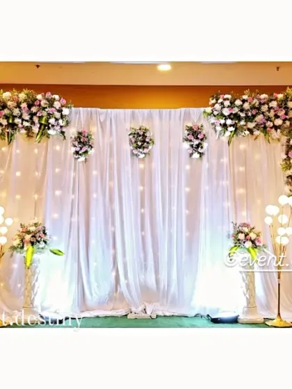 For a clean and sophisticated look, we created this all-white stage with fairy lights embedded in the drapes. The setup is framed by lush floral arrangements on the corners and floor, perfect for an elegant engagement party.