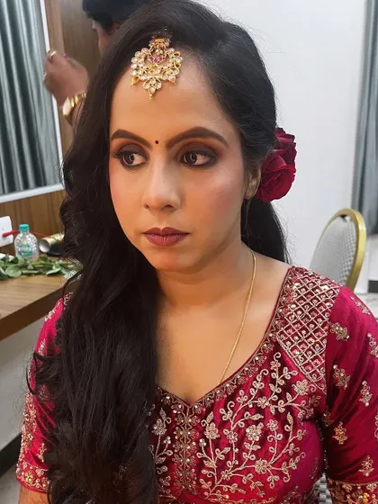 A beautiful reception look in red. The makeup features a warm, smokey eye and a matching red lip, complemented by soft waves and a fresh rose in her hair.