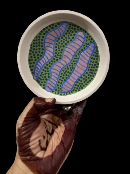A hand-painted plate with a playful pattern of green dots and pink-and-blue worms. I don't take my patterns too seriously; the goal is to create something that makes you smile.