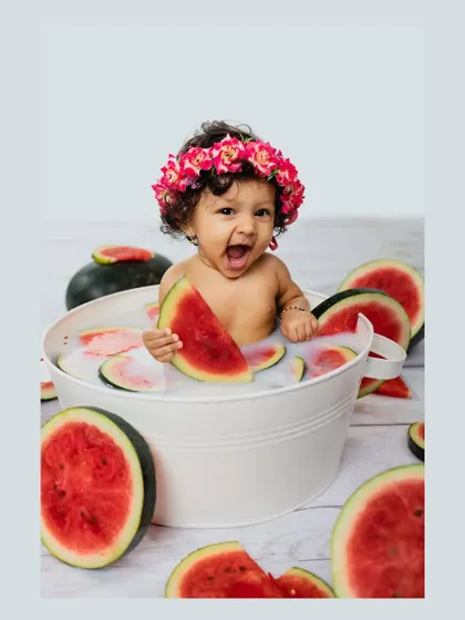 A baby girl laughs with delight while holding a slice of watermelon in her milk bath. Her joyful expression is the highlight of this fun and fruity photoshoot.