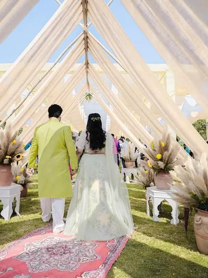 The couple's entrance at their bohemian-themed Mehendi, walking down a carpeted aisle through a tunnel of soft drapes and pampas grass.