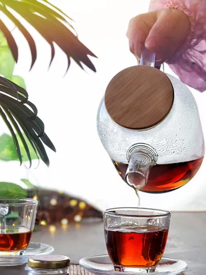 A perfect pour of black tea into a clear glass cup. The human element and the bright, clean lighting give this shot a fresh and inviting feel, ideal for a tea brand.