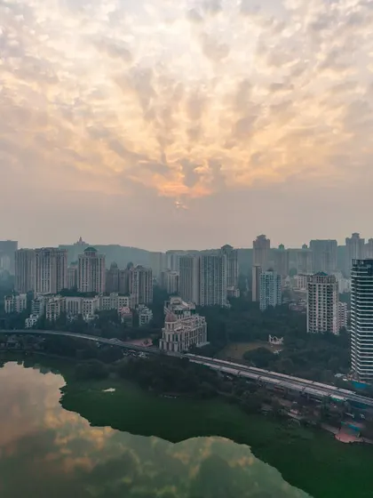 An aerial view of the Powai skyline at sunset, with the clouds catching the last light and reflecting in the lake.