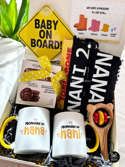 This hamper for the 'Nana' and 'Nani' to be includes personalized mugs, a 'Baby on Board' sign, a wooden rattle, and sweet treats to celebrate their new roles.