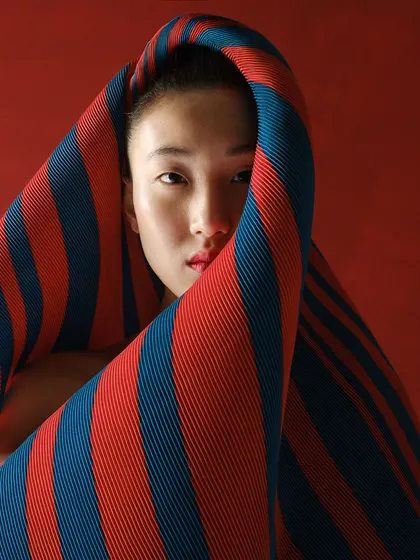 A close-up portrait where the model is enveloped by the striped pleated fabric. This shot focuses on the texture and color of the textile as a primary design element.