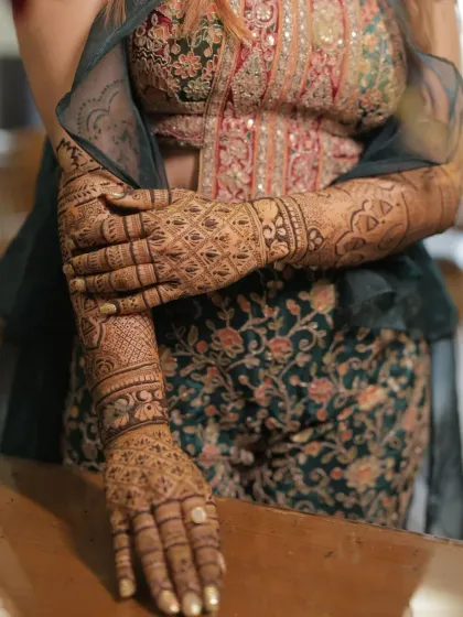 A close-up of a bride's hands, showing a very detailed and intricate full-coverage mehendi. The design is so dense that it looks like lace gloves.