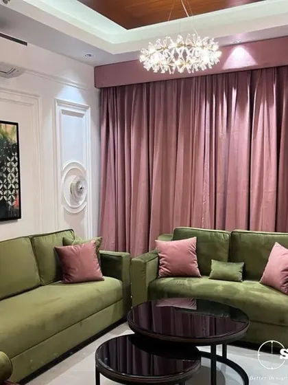 Another angle of the colorful living room, showing the interplay between the olive sofas and the long, flowing pink curtains. The crystal chandelier adds a touch of glamour to the eclectic space.