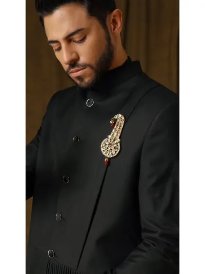 A detailed shot of the 'Vishudh' bandhgala, focusing on the ornate, handcrafted brooch. This accessory elevates the classic black jacket, making it suitable for the most formal of occasions.