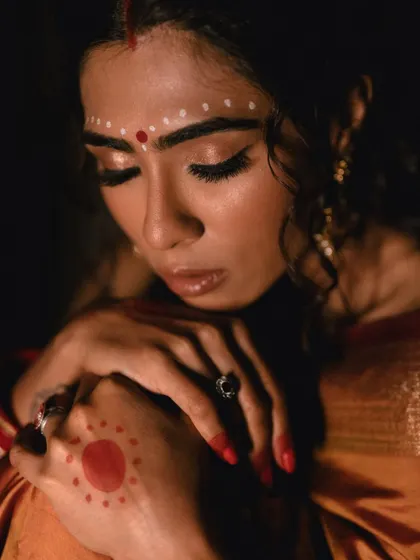 A close-up, contemplative portrait. The focus is on the model's serene expression and the delicate alta designs on her hand, creating a soulful and artistic image.