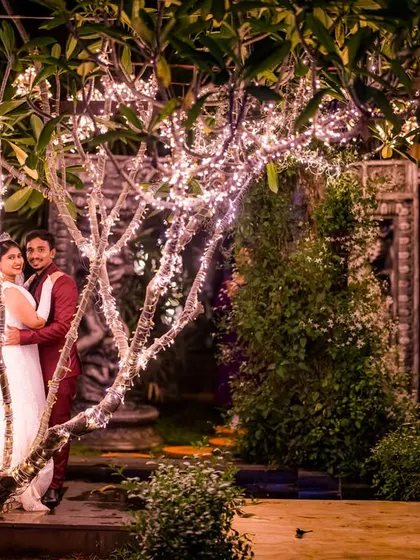 A couple shares a quiet moment under a tree adorned with fairy lights. This setup creates a whimsical and enchanting backdrop for a romantic night shoot.