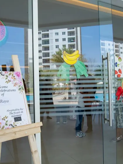 The welcome setup for Raya's fruit-themed first birthday. A custom sign on an easel, paired with themed window decals, greets guests at the entrance to the party venue.
