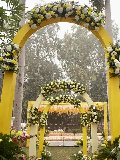 The yellow floral arches create a beautiful, layered entrance, inviting guests into the garden where the Haldi ceremony will take place.