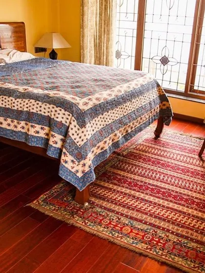 In this bedroom at the Roopa Hariprasad Residence, a carved wooden headboard and traditional textiles create a serene and culturally rich environment. The large window with its decorative grille allows for ample light while maintaining privacy.