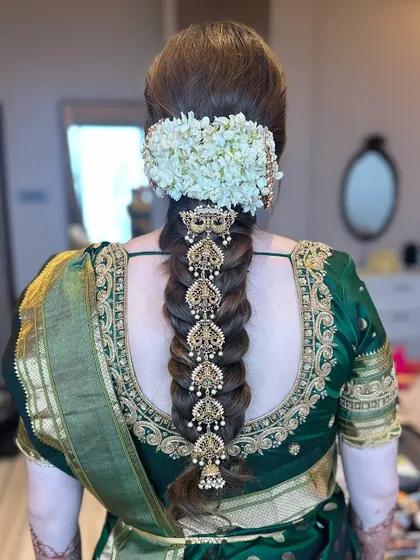 A detailed view of a traditional South Indian bridal braid, showcasing the beautiful contrast between fresh jasmine flowers and intricate gold temple jewelry hair accessories (Jadanagam). This style is a testament to timeless bridal beauty.