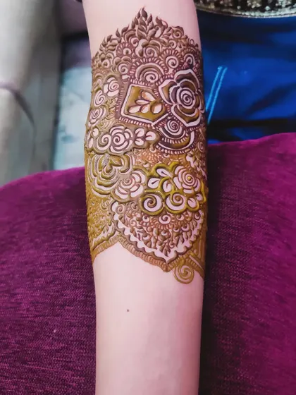 A close-up of a floral and paisley arm band, showing the texture and precision of the fresh henna paste.