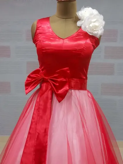 A detailed view of our red and pink gown, featuring a satin bodice with a large bow and a layered tulle skirt. The shoulder is accented with a white floral piece, adding a unique touch.