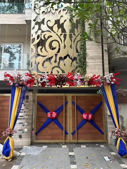The entrance gate of a modern house decorated for a wedding. The gate is adorned with blue and yellow drapes and a large floral arrangement on top.