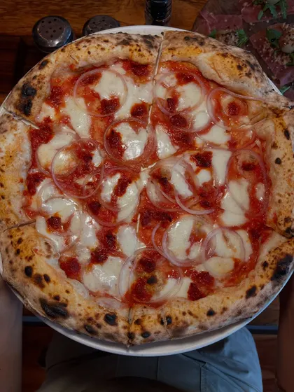 Holding up the Goan Sausage pizza. It's a full meal and an experience in one.