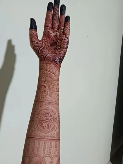A full arm view of a bridal henna design, showcasing the journey from fingertips to elbow. The pattern includes mandalas, paisleys, and traditional bands, creating a cohesive and stunning piece of art.