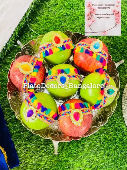 A mix of red and green apples decorated with colorful braided ribbons and kundan stones, creating a festive and eye-catching fruit platter.