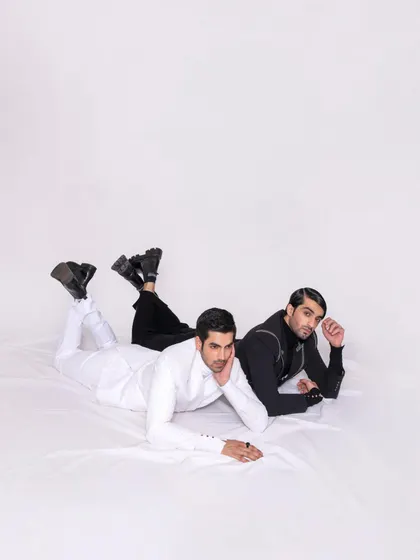 A creative composition featuring two models in contrasting black and white suits. The overhead shot and relaxed poses create a visually interesting editorial image that showcases both outfits.