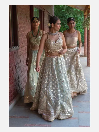 A group shot of three models walking in a line, showcasing a collection of pastel-colored lehengas by Vandana Sethi. This image is effective for lookbooks and campaigns that need to display multiple pieces from a collection.