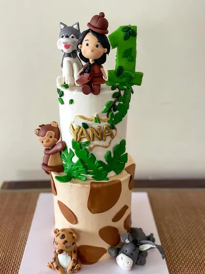 Yana's 1st birthday cake, featuring all her favorite animals! This two-tiered cake has a giraffe print bottom and is adorned with a custom girl figurine and several handmade animal friends.