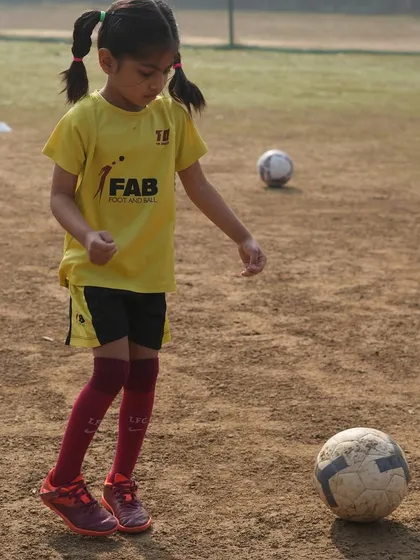 A young player with pigtails stands over the ball. The football field is a classroom, and every session is a lesson in teamwork, perseverance, and strategic thinking.