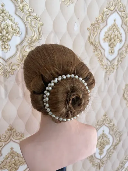 A classic rose bun surrounded by a string of pearls. This timeless hairstyle is a favorite for brides and is a key part of our bridal hairstyling curriculum.