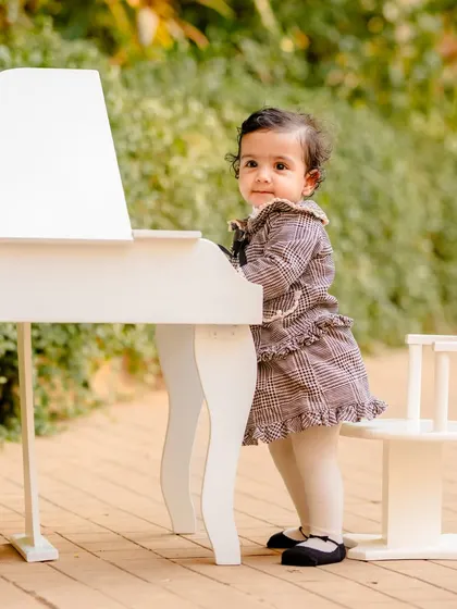 A full-length view of a little girl in a plaid dress playing with a white miniature piano outdoors.
