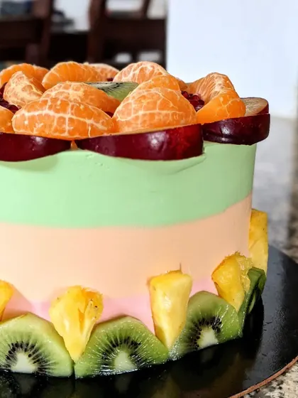 A close-up view of the side of the fresh fruit cake, showing the neat arrangement of kiwi and pineapple slices.