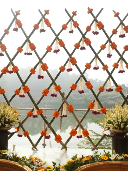 A full view of the bamboo lattice backdrop for a lakeside Haldi, decorated with marigold bunches and hanging floral tassels.
