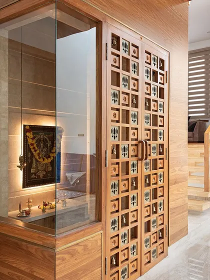 The pooja room in the Cube House is enclosed in glass, making it a visual feature of the home. The custom-designed wooden doors with small bells and motifs add a unique, handcrafted touch to the modern design.