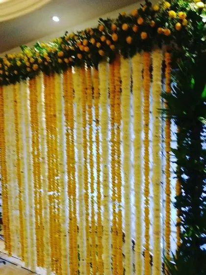 A close-up of a floral wall made from alternating strings of yellow and white flowers, framed with greenery.